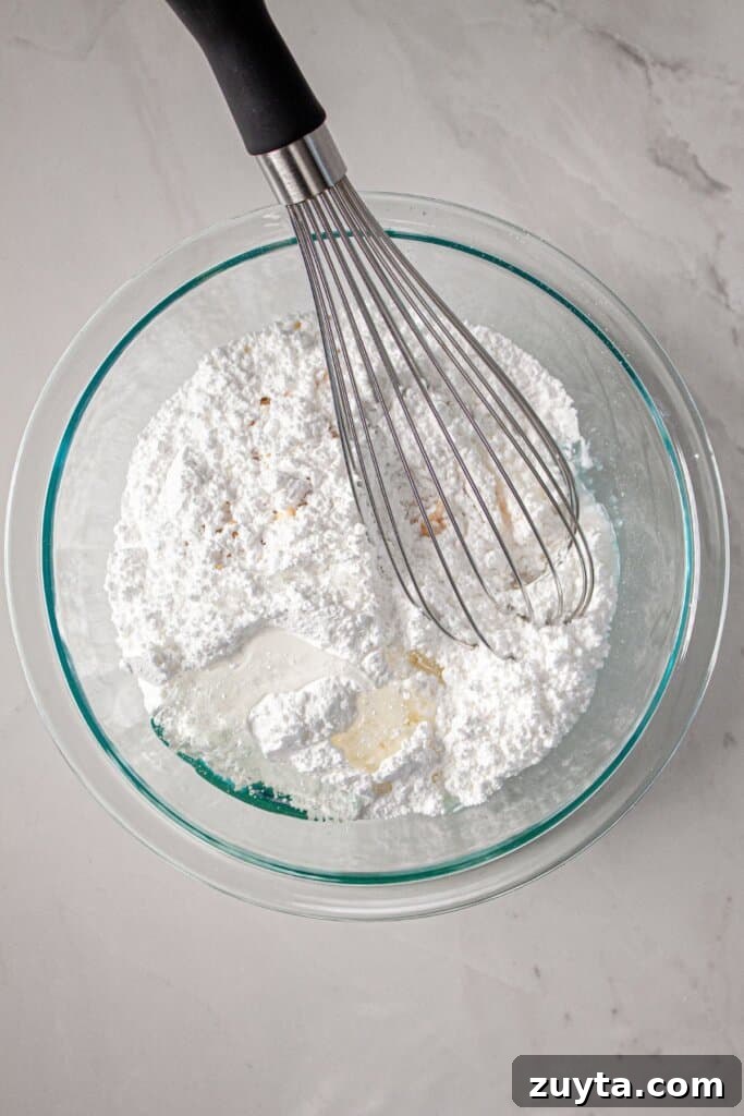 Powdered sugar and wet ingredients being mixed in a glass bowl.