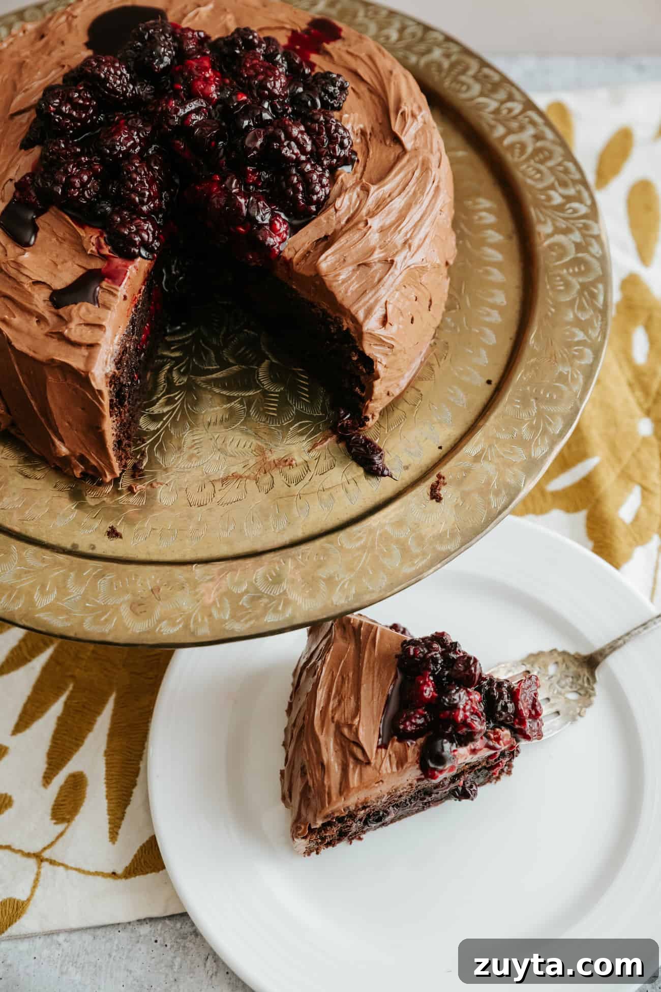overhead shot of double layered chocolate cake on a golden platter with a slice taken out. THe cake is garnished with roasted berries and frosted in mocha buttercream.