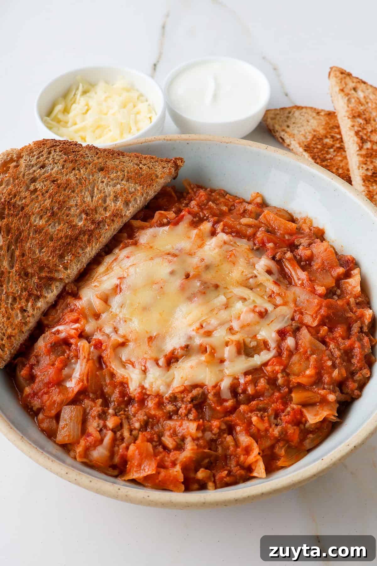 Spicy Chipotle Ground Beef and Cabbage Casserole Recipe 9 Side shot of casserole in a bowl with melted cheese and bread on the side.
