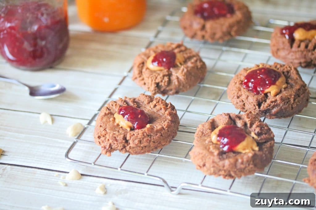 Flourless Peanut Butter and Jam Cookies (Dairy-Free Recipe) 9 Cooling rack with flourless peanut butter thumbprint cookies topped with jam with a jar of jam and a spoon behind them