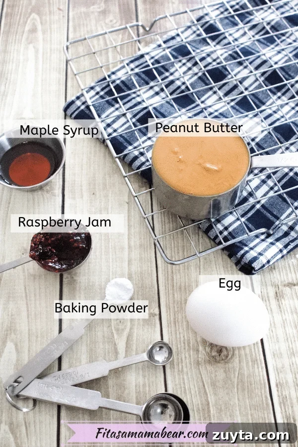 Flourless Peanut Butter and Jam Cookies (Dairy-Free Recipe) 3 Cooling rack on a blue linen with a measuring cup of peanut butter on it and multiple measuring spoons and an egg around it