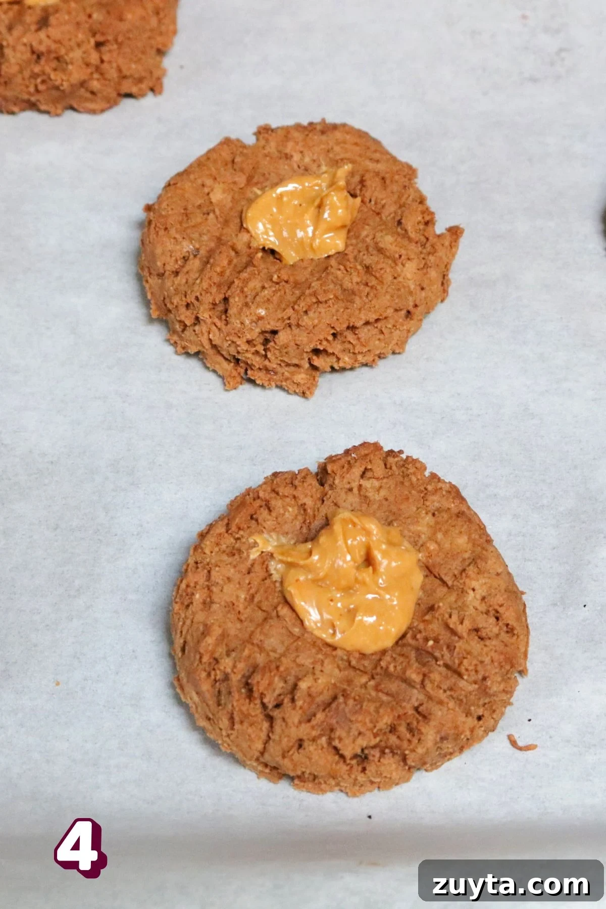 Flourless Peanut Butter and Jam Cookies (Dairy-Free Recipe) 7 Flourless peanut butter cookies on parchment paper topped with peanut butter.