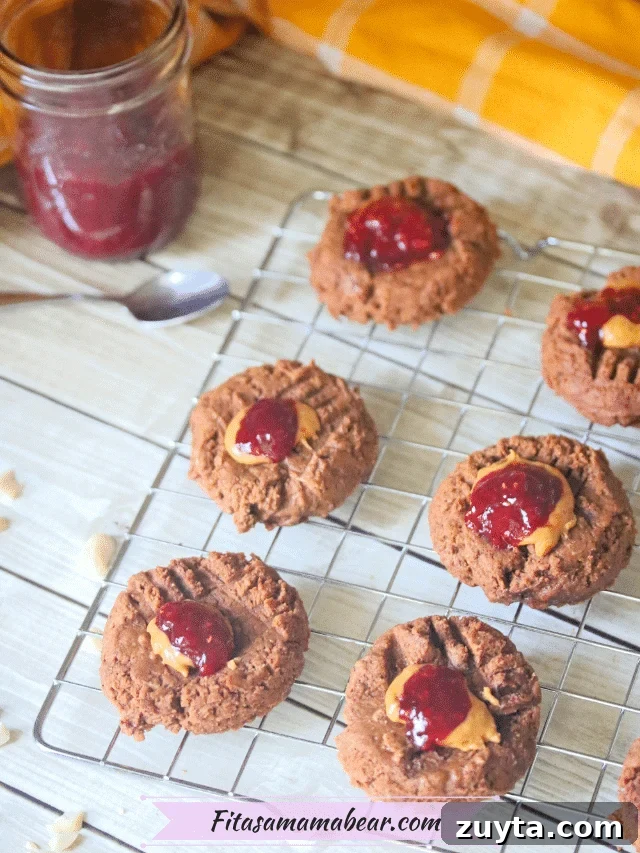 Flourless Peanut Butter and Jam Cookies (Dairy-Free Recipe) 8 Cooling rack with flourless peanut butter thumbprint cookies topped with jam with a jar of jam and a spoon behind them
