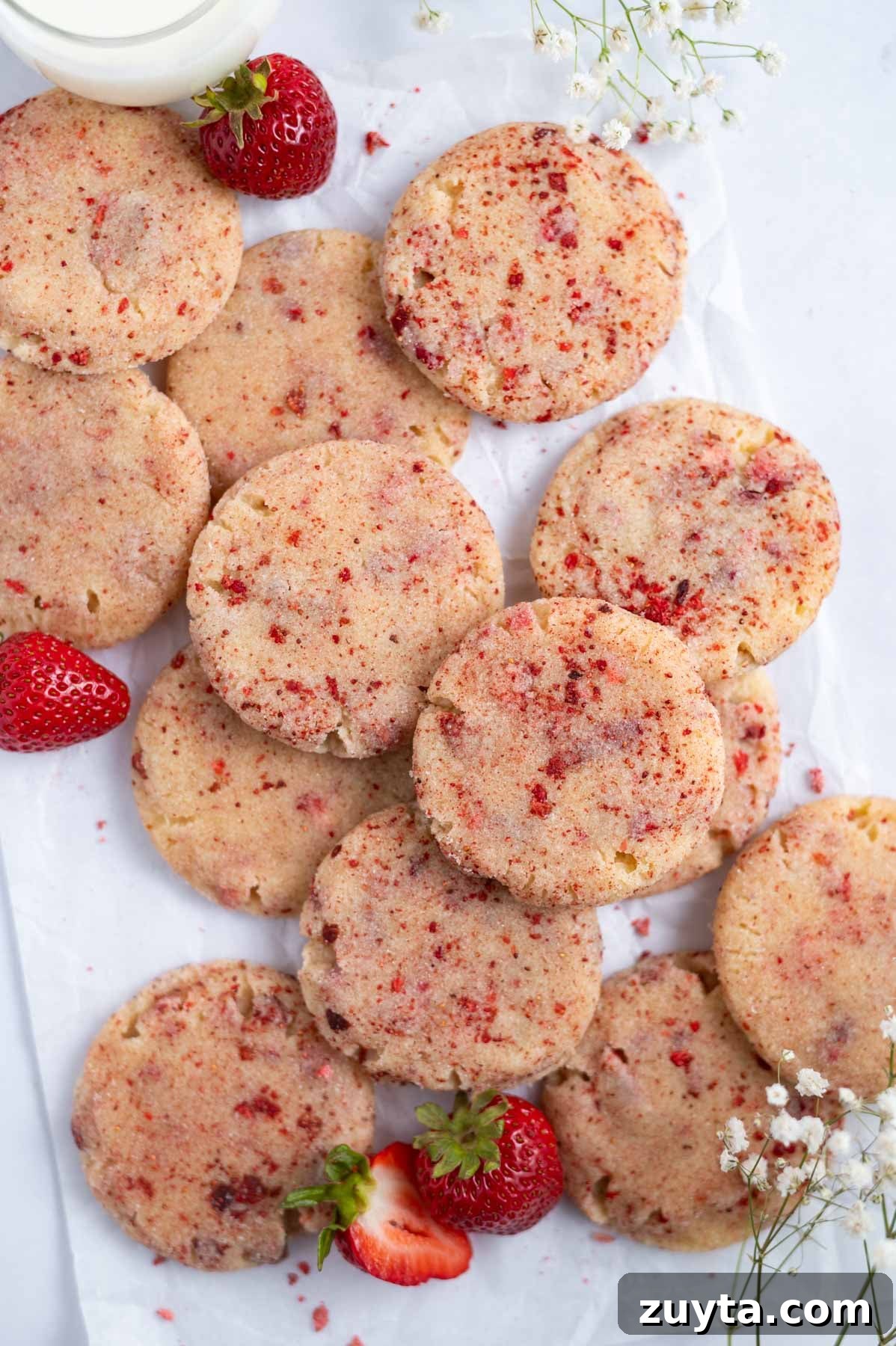 pile of cookies on parchment paper with fresh strawberries and a glass of milk