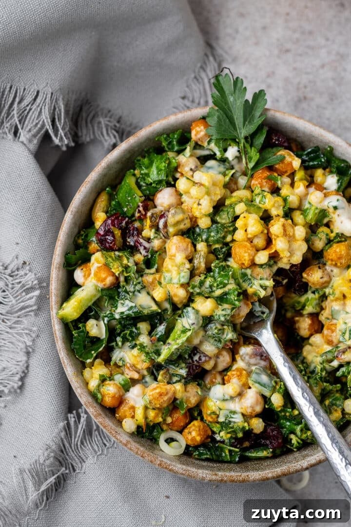 closeup view of a fork scooping up kale, chickpeas, cucumbers and pearl couscous