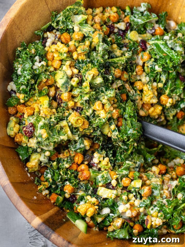 large wooden bowl full of kale and couscous salad with a large black spoon scooping it up