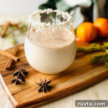 What to Use Instead of Sweetened Condensed Milk 5 a glass of coquito with a coconut rim on a wood cutting board surrounded by spices, oranges and rosemary