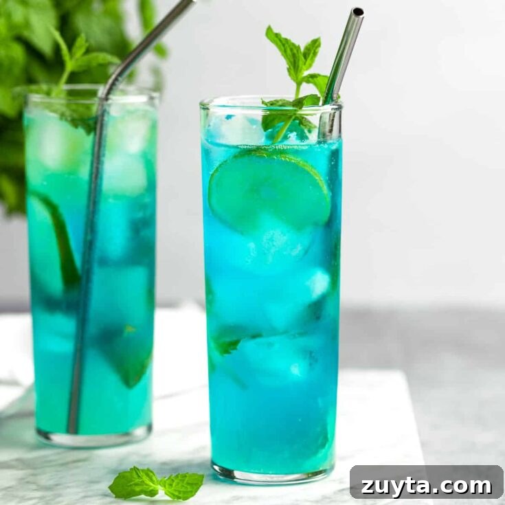 A couple blue mojitos garnished with lime slices and mint leaves.