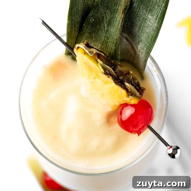 Overhead view of a pina colada with coconut milk, garnished with a pineapple slice and a maraschino cherry.