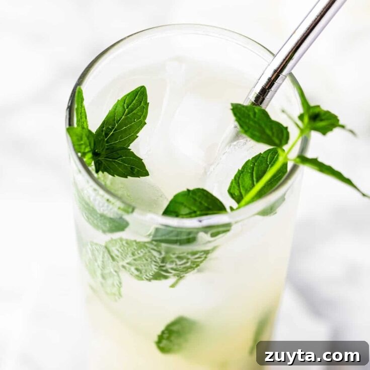 A lychee mojito garnished with fresh mint, on a white marble table.