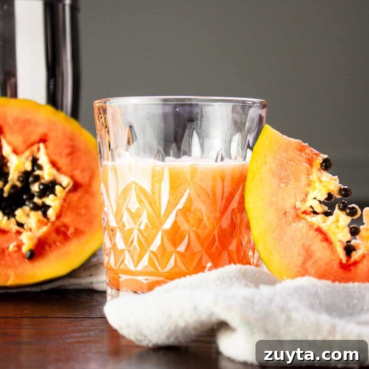 Glass of papaya rum punch beside half a papaya and a papaya slice