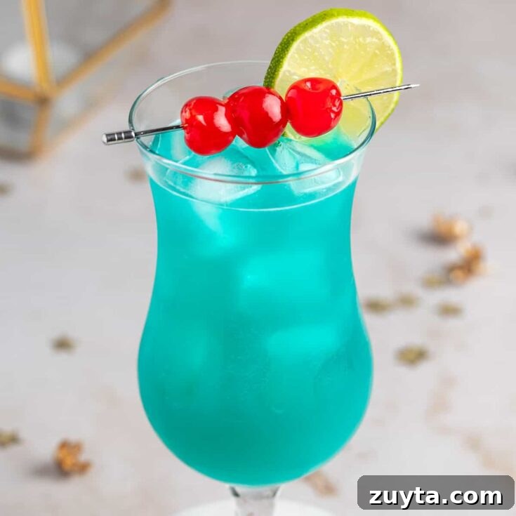 A blue hurricane drink garnished with maraschino cherries and a lime slice, on a marble table.