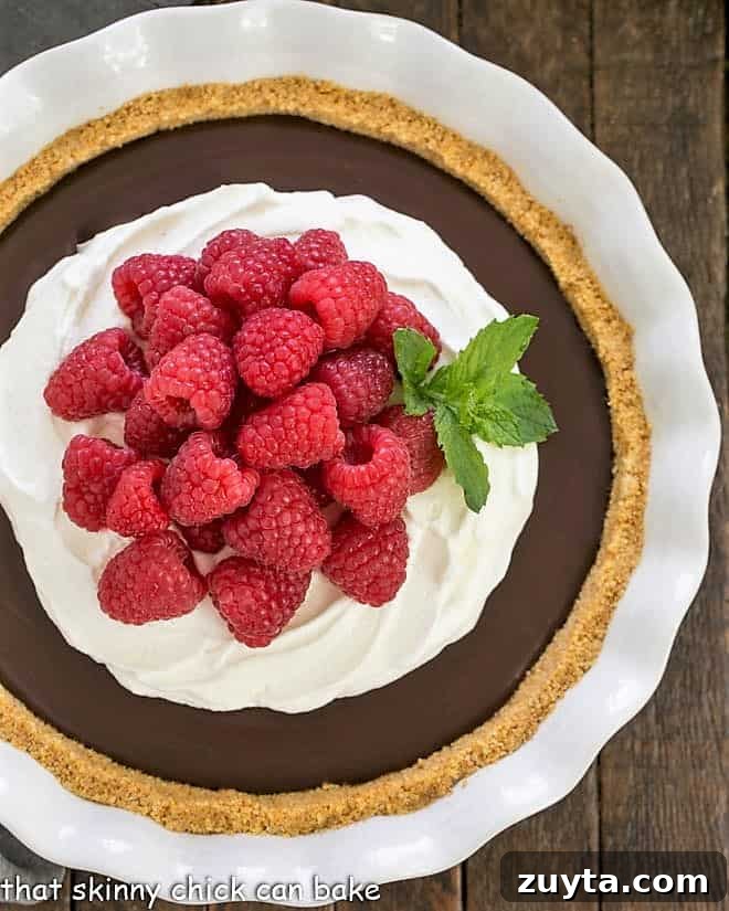 Chocolate Satin Pie - Dreamy dark chocolate filling in a graham cracker crust! Overhead view of dark chocolate satin pie in a ceramic pie plate topped with raspberries and whipped cream.