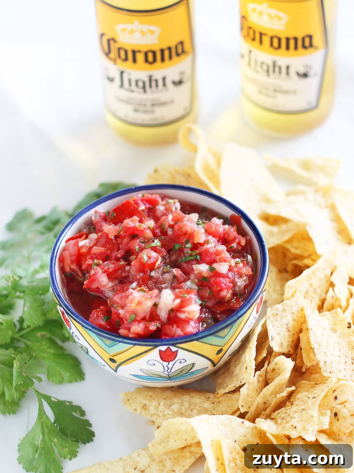 Garden Fresh Salsa Recipe with Tomatoes and Herbs 2 Fresh garden salsa in a decorative bowl, surrounded by tortilla chips and two bottles of Mexican beer in the background.