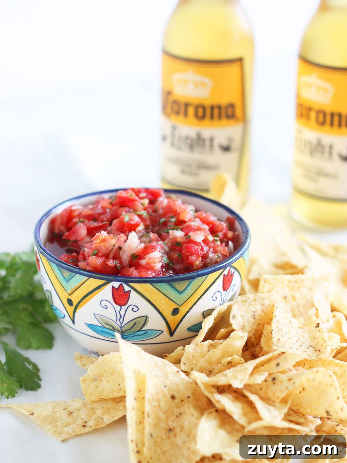 Garden Fresh Salsa Recipe with Tomatoes and Herbs 17 Fresh garden salsa in a decorative bowl, surrounded by tortilla chips and two bottles of Mexican beer in the background.