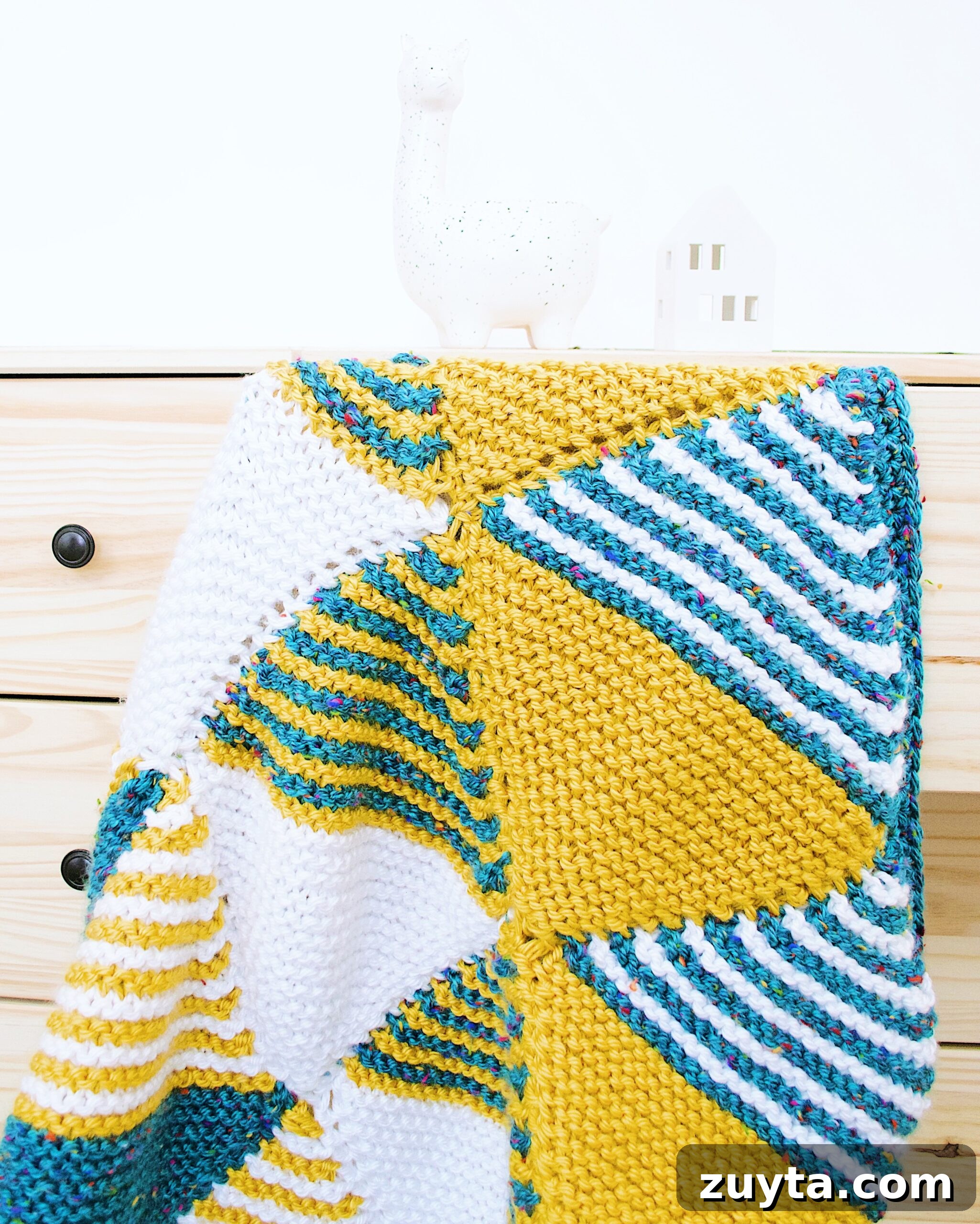 The Knitted Baby Blanket draped over a wooden set of drawers