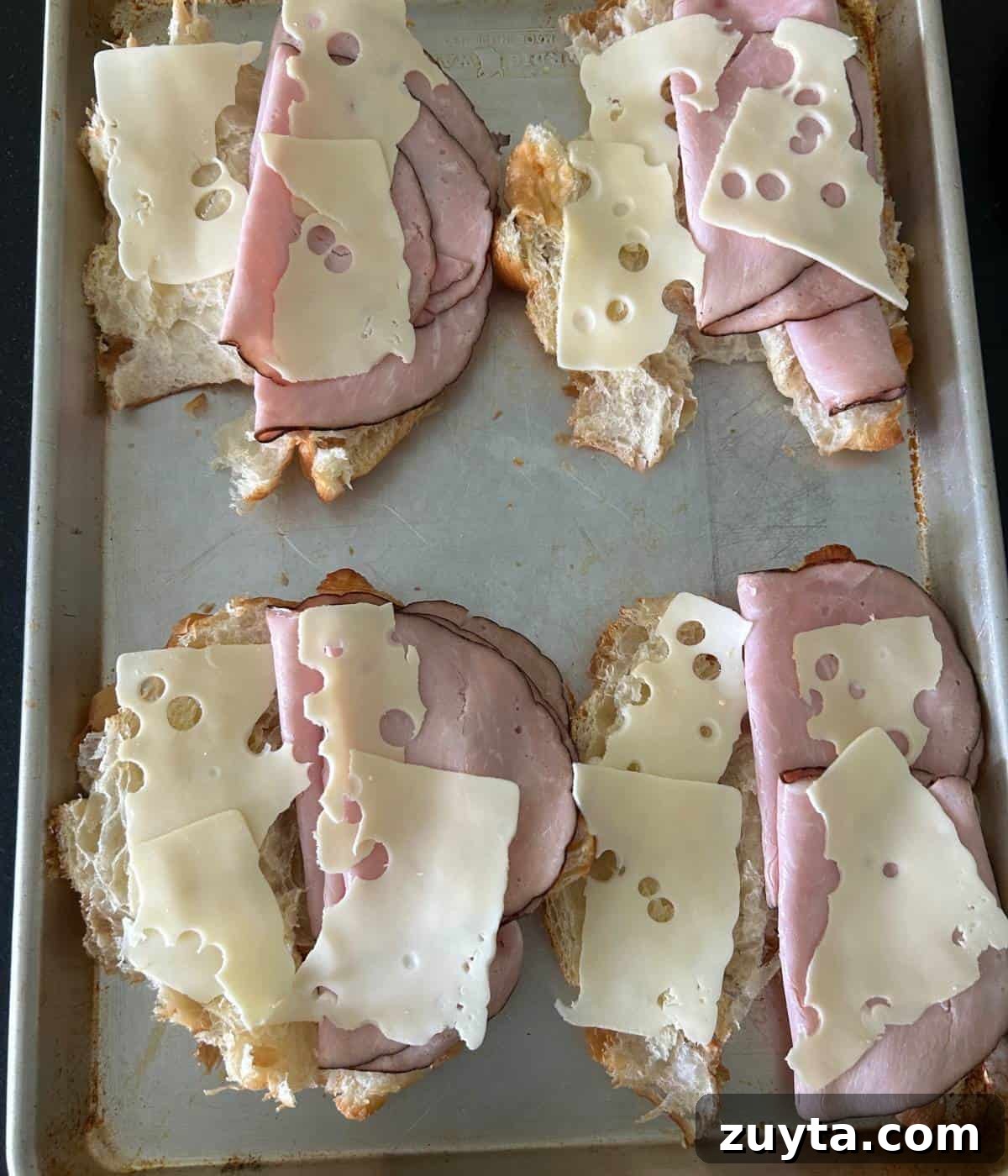 Croissants with ham and cheese on cookie sheet.