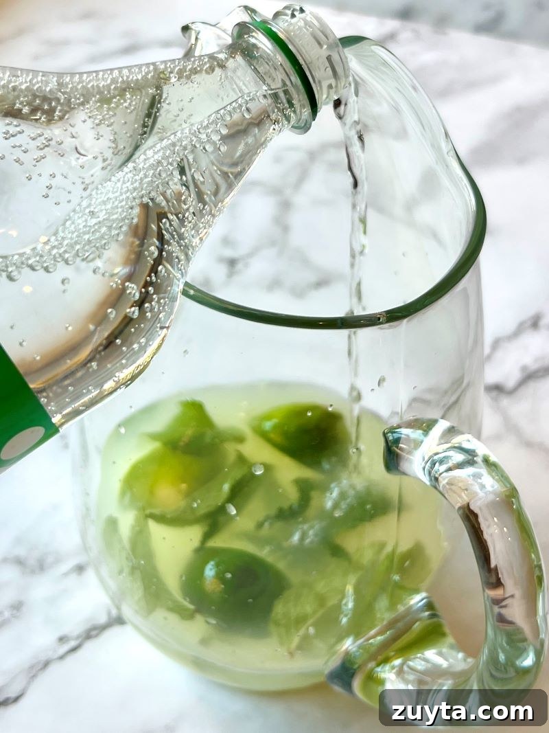Virgin Mojito Recipe: Mint and Lime Mocktail 5 Adding sprite to a glass pitcher with lemonade mix, limes and mint.