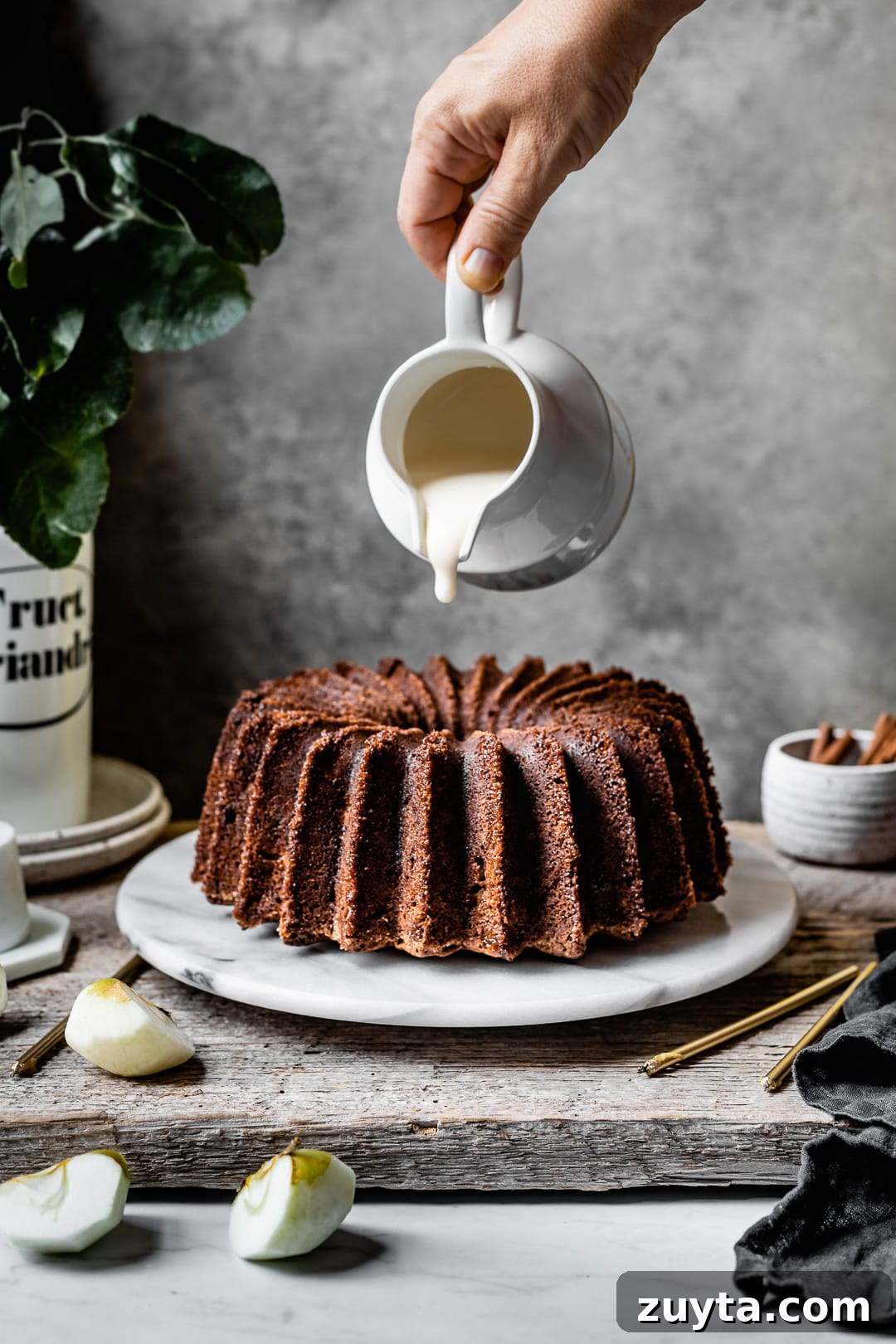 Moist Applesauce Bundt Cake Recipe with Cinnamon Glaze 4 Hand pouring white glaze onto an apple bundt cake