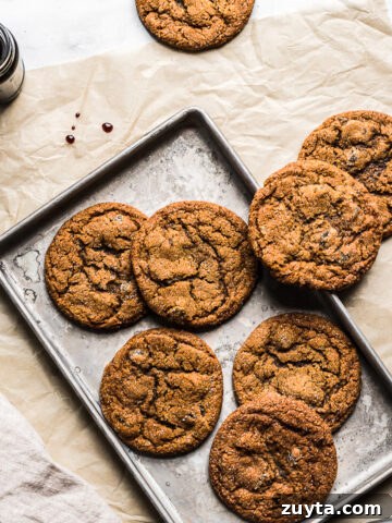 Ginger cookies on a baking sheet resting on a brown parchment paper rectangle. A jar of molasses is nearby.