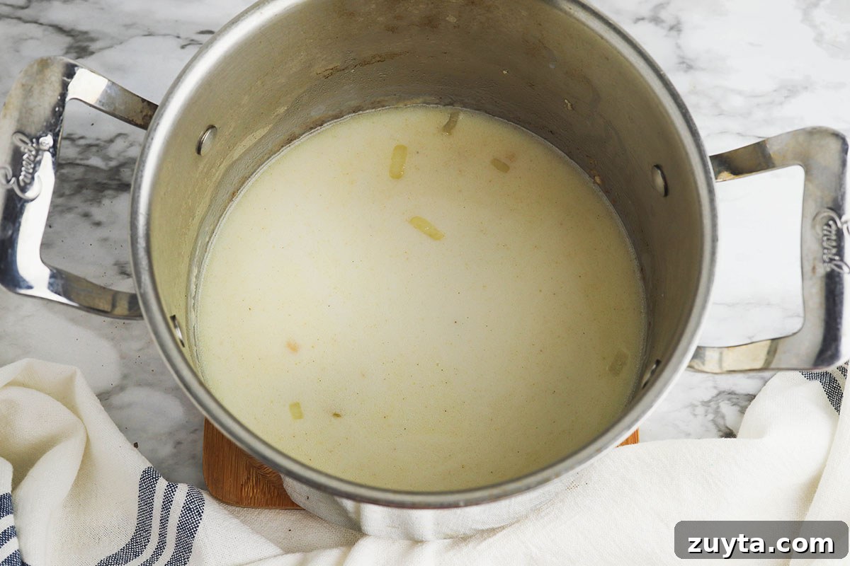 Creamy Cheesy Ham and Potato Casserole 8 Chicken broth and milk are added to the ingredients in the saucepan.