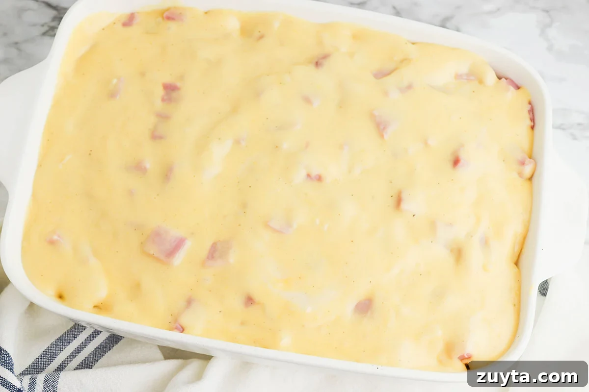 Creamy Cheesy Ham and Potato Casserole 10 Cheese sauce is poured over the ham and potatoes in the casserole dish.