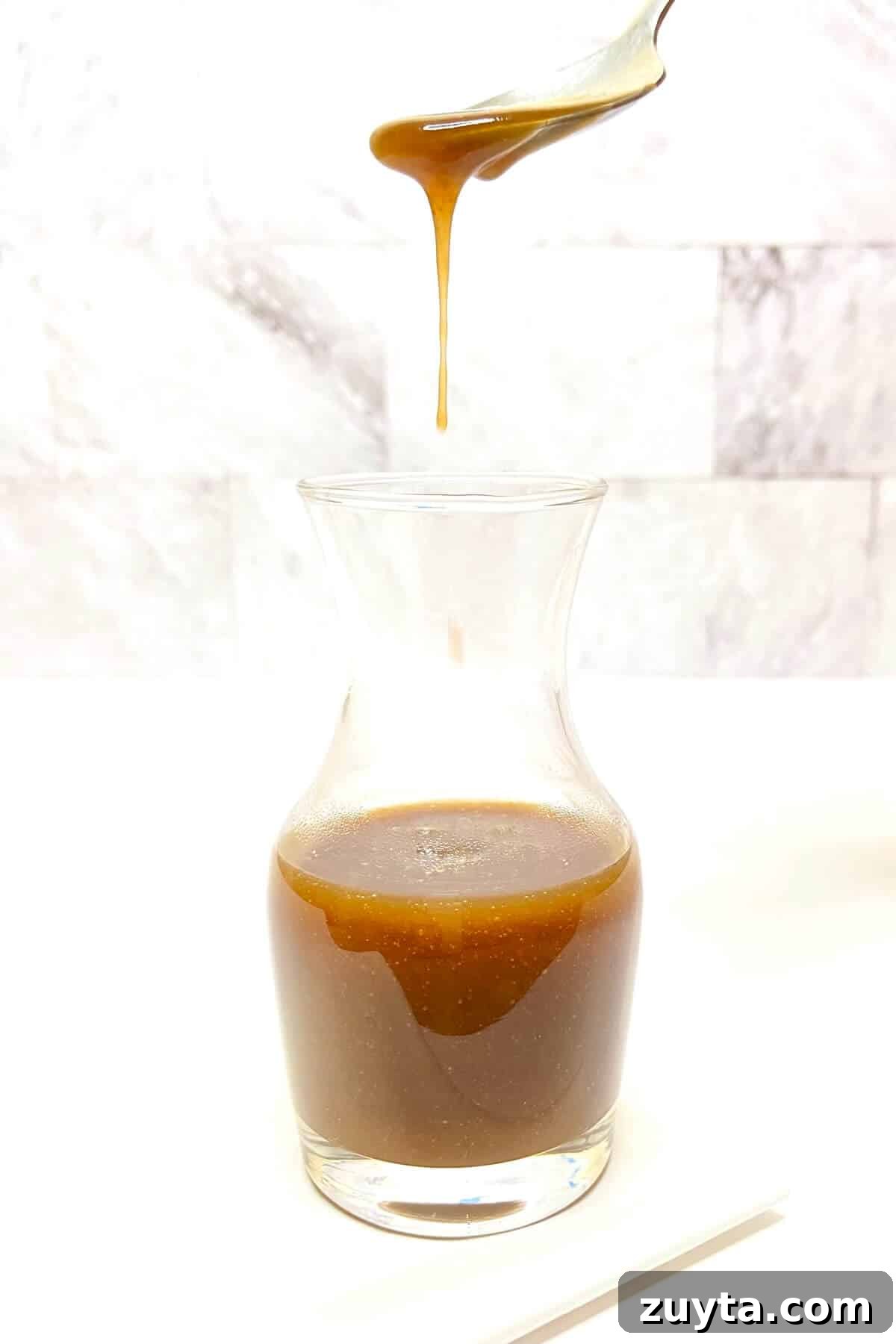 Creamy Butterscotch Milkshake Recipe 6 Caramel sauce dripping off of a spoon into a small carafe of sauce.