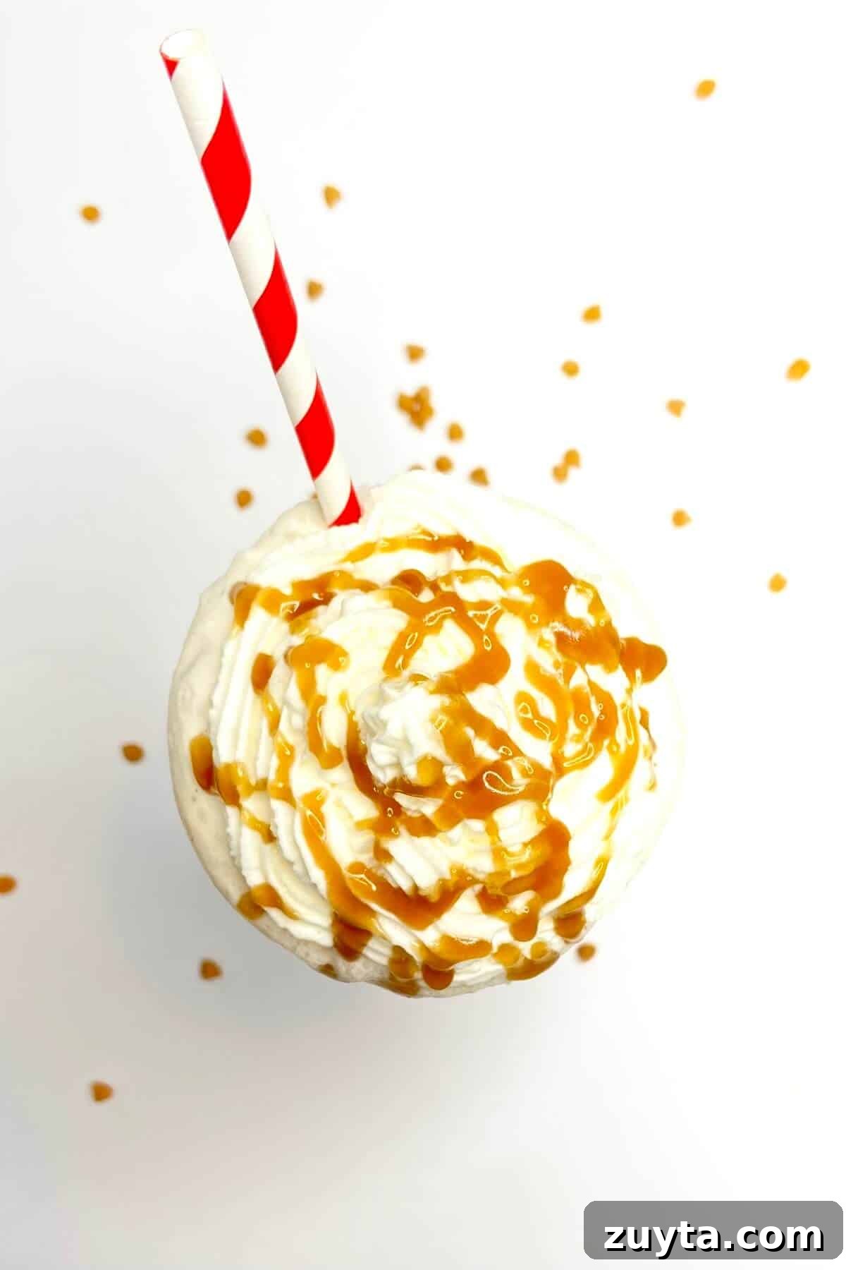 Creamy Butterscotch Milkshake Recipe 7 Milkshake on white table, with caramel chips sprinkled around.
