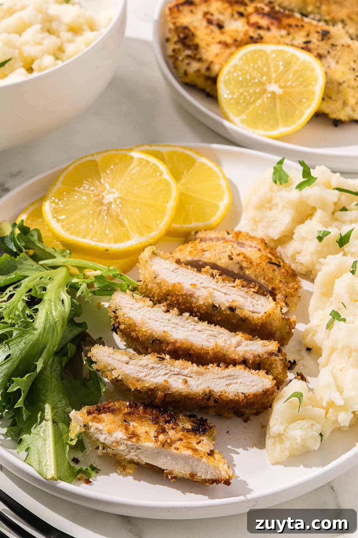 Crispy Italian Chicken Cutlets Recipe 2 A plate with Italian chicken cutlets, salad, mashed potatoes and lemons.