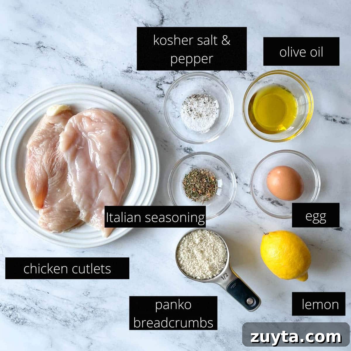 Crispy Italian Chicken Cutlets Recipe 3 The labeled ingredients for Italian Chicken Cutlets sit on a white marble counter; they include: chicken cutlets, olive oil, kosher salt, pepper, Italian seasoning, an egg, a lemon, and panko breadcrumbs.