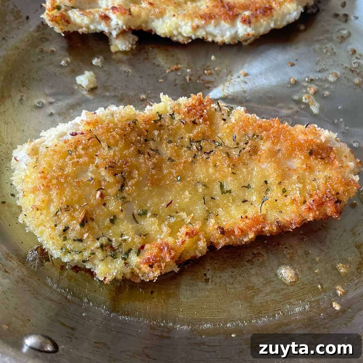 Crispy Italian Chicken Cutlets Recipe 7 Fried, breaded chicken cutlet cooking in a stainless steel frying pan.