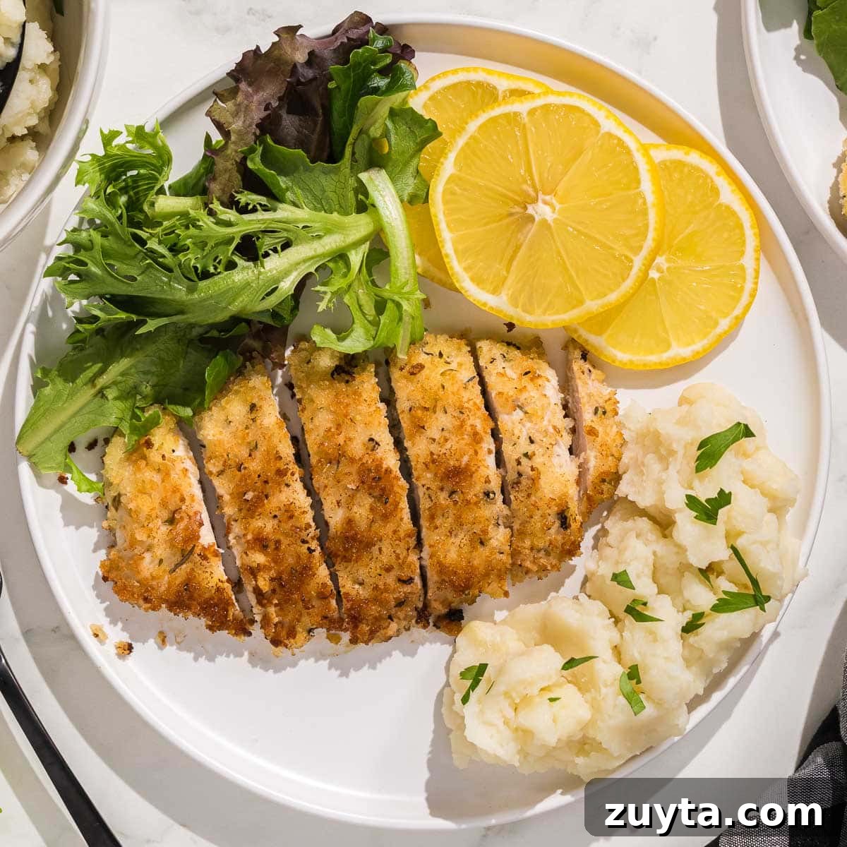 Crispy Italian Chicken Cutlets Recipe 8 A plate of Italian chicken cutlets, mashed potatoes and lemons.