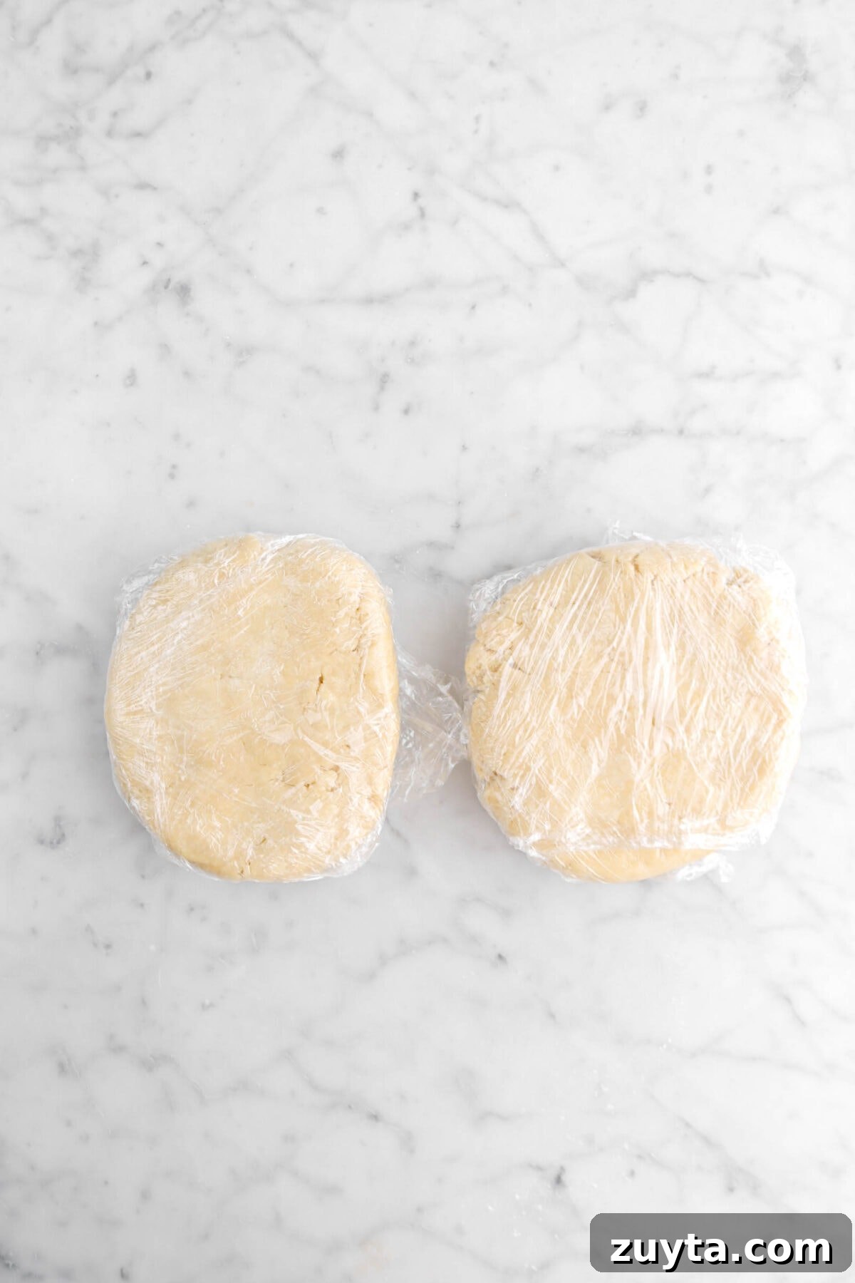 Cinnamon-Spiced Peach Hand Pies Recipe 7 two pieces of dough wrapped in plastic wrap on marble surface