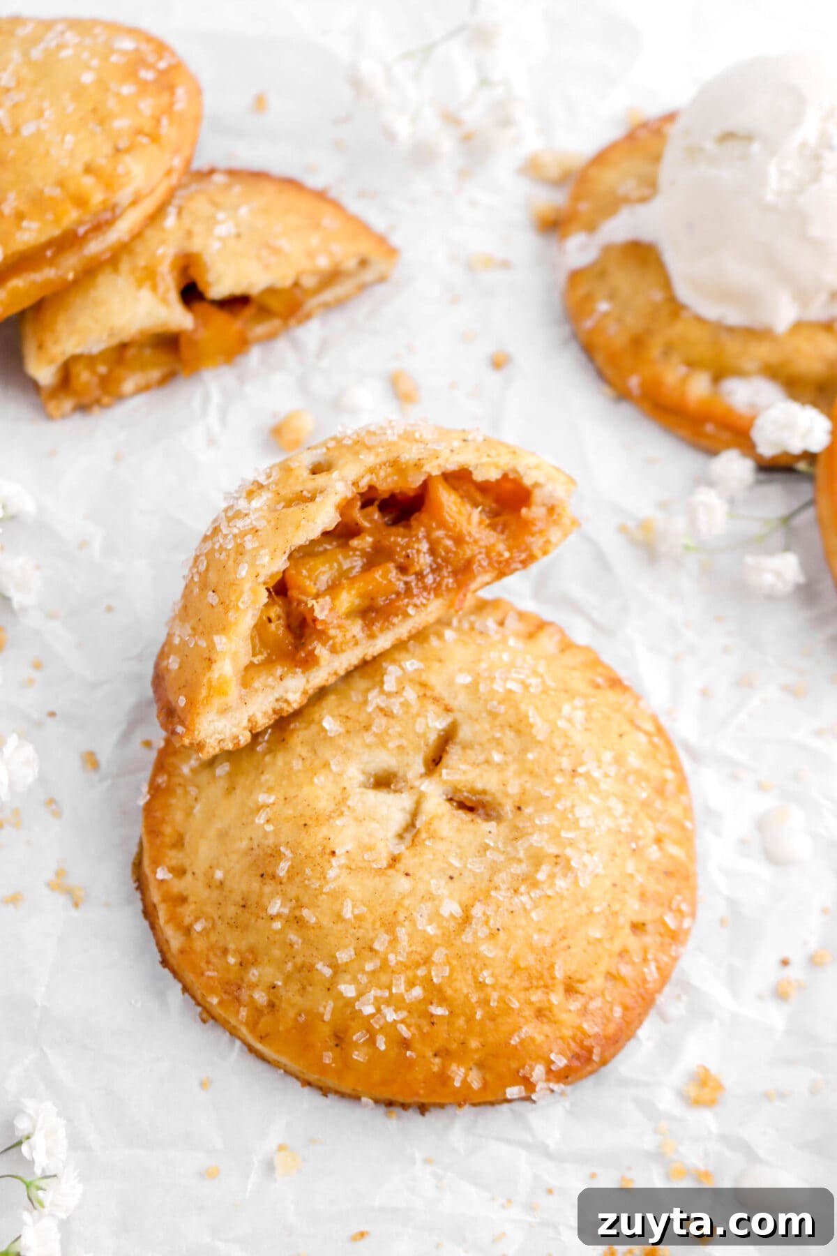 Cinnamon-Spiced Peach Hand Pies Recipe 12 angled shot of peach hand pie on parchment with one cut in half leaning against it