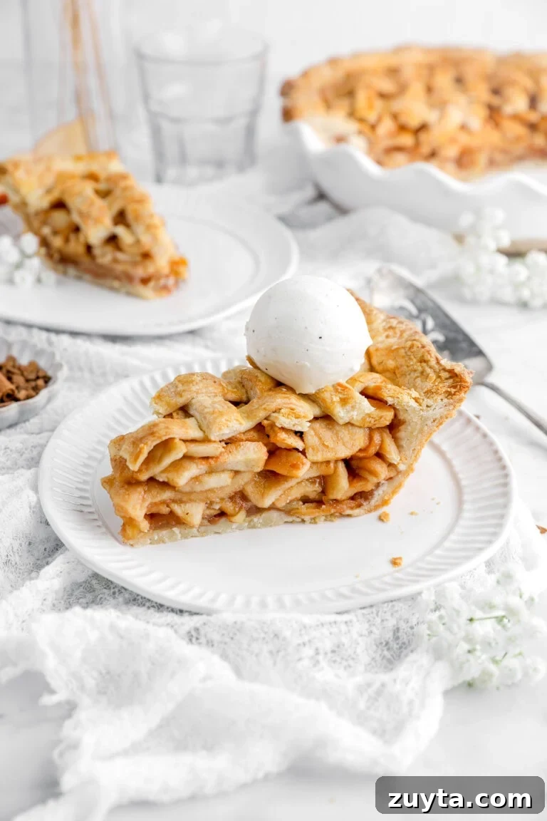 slice of apple pie with ice cream scoop on top and another slice of pie behind.