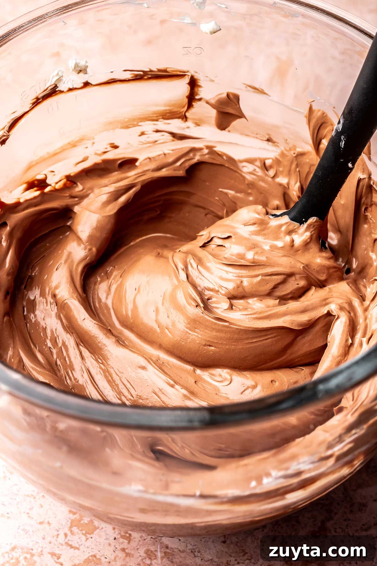 Silky Chocolate Swiss Meringue Buttercream Recipe 11 A spatula sits in a bowl of chocolate swiss meringue buttercream.
