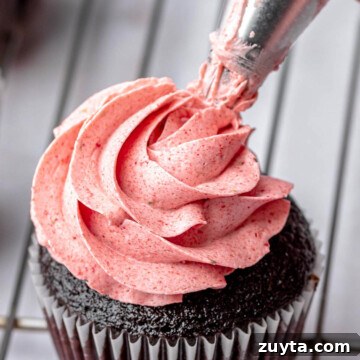 A piping bag pipes strawberry swiss meringue buttercream on a cupcake.