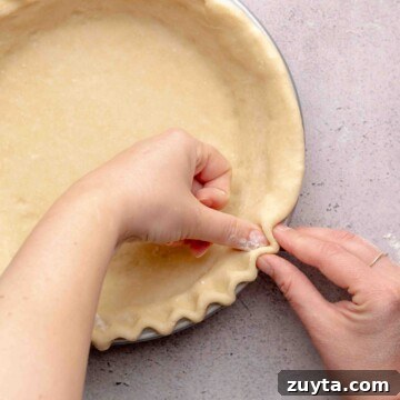 Two hands crimping edges of pie dough.