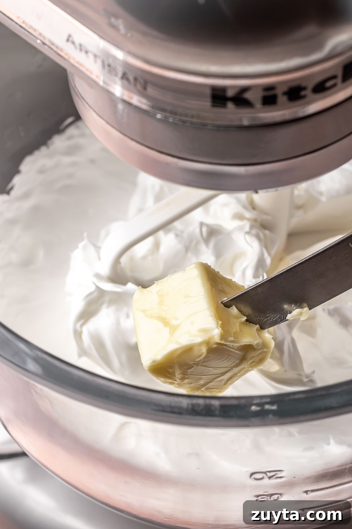 Silky Chocolate Swiss Meringue Buttercream Recipe 6 A knife adds butter into a bowl of swiss meringue.
