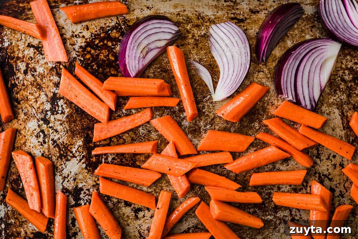 Maple-Roasted Carrots and Dates with Pistachio Pesto 5 Carrots and onions on a baking sheet before being roasted.