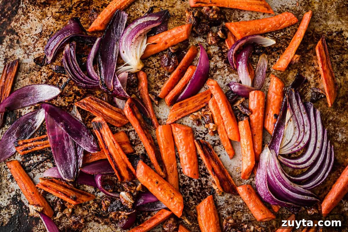 Maple-Roasted Carrots and Dates with Pistachio Pesto 6 Carrots and onions on a baking sheet after being roasted.