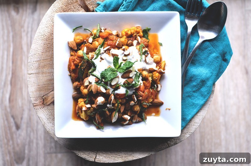 Top down view of Moroccan Vegetable Stew With Dried Figs and Fresh Mint on a blond wooden table with blue cloth napkin.