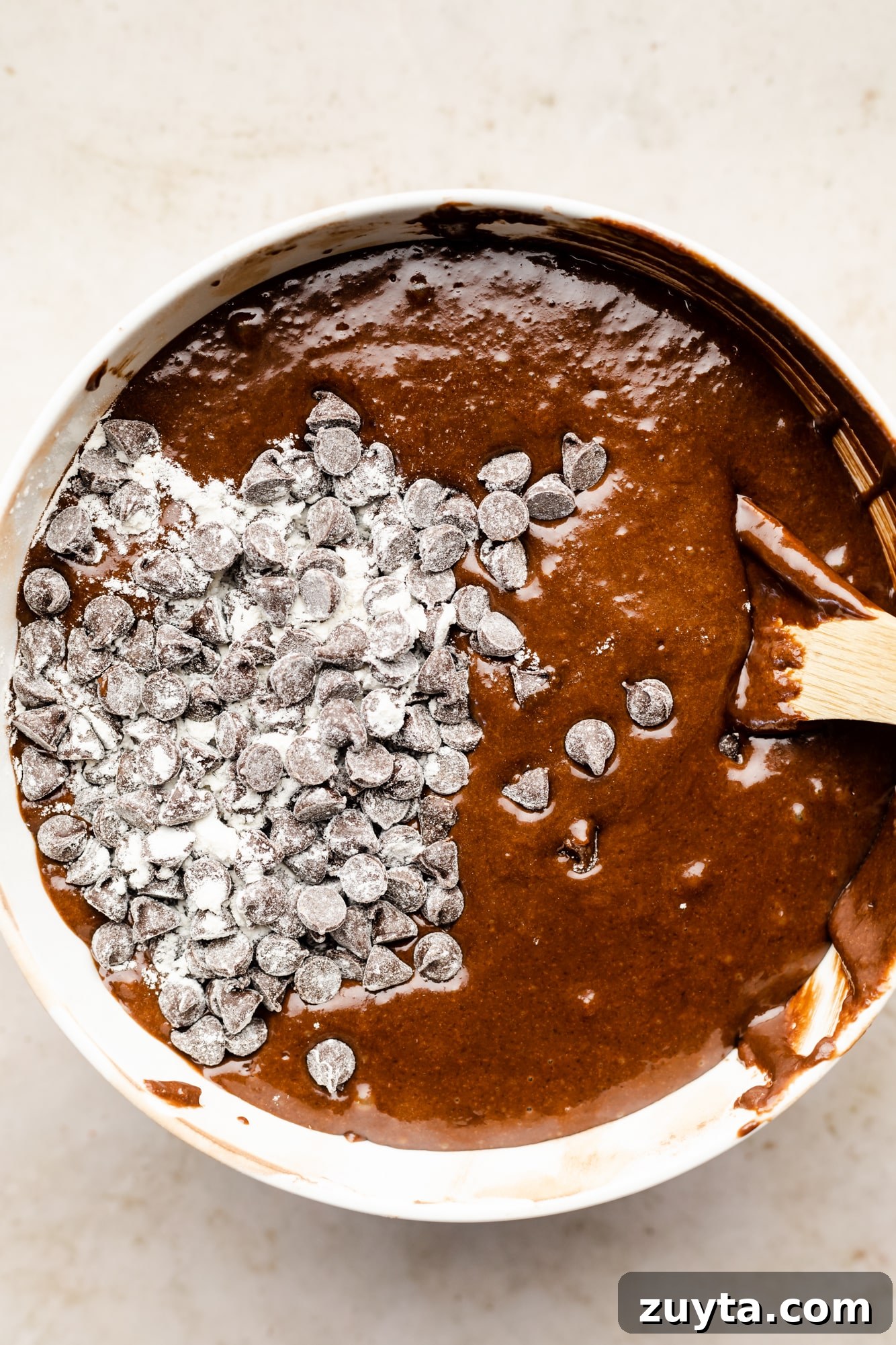 using a wooden spoon to fold chocolate chips into chocolate cake batter.