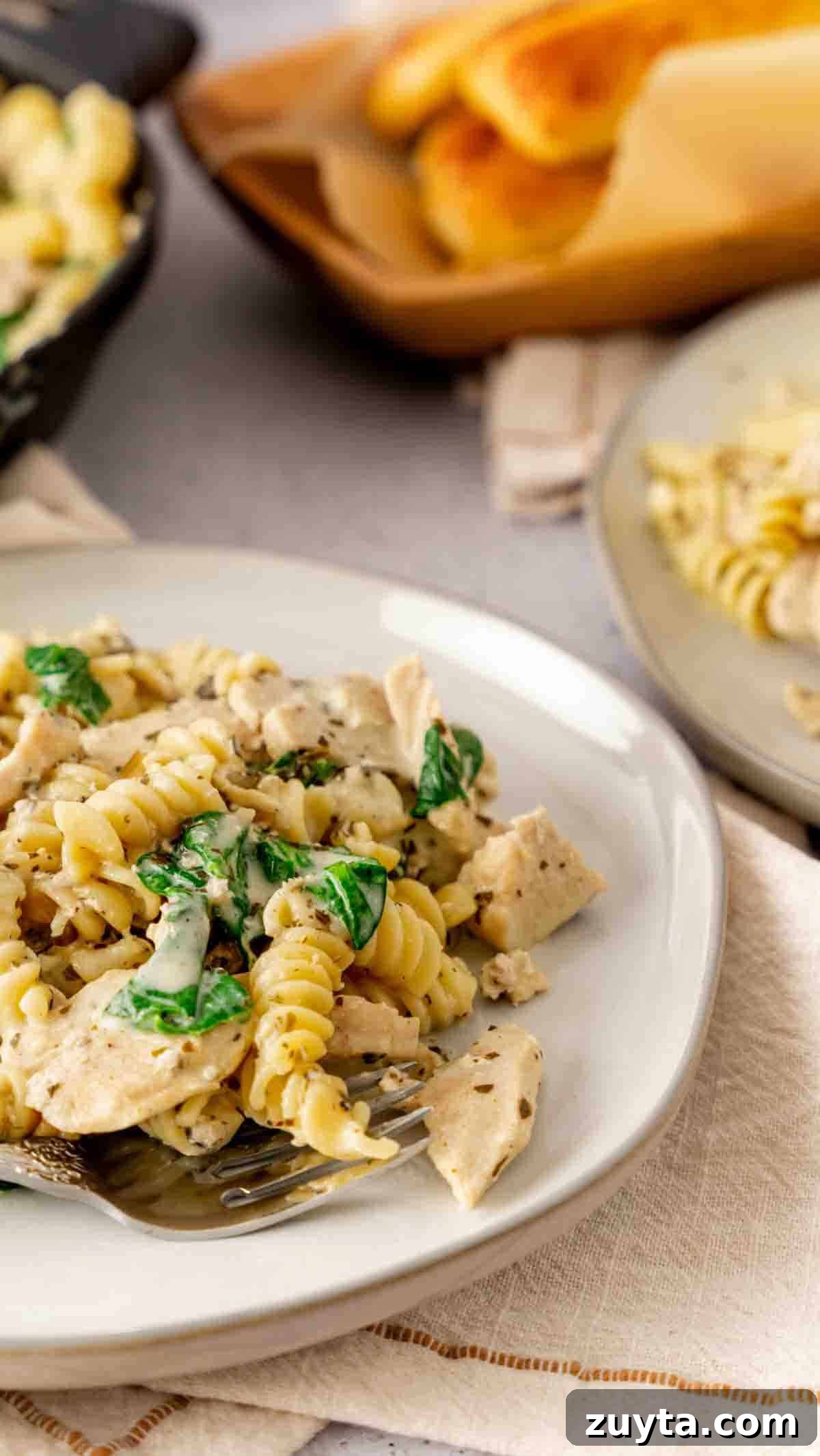 Instant Pot Creamy Pesto Chicken Pasta 3 A plate of chicken pesto pasta made in the Instant Pot with a serving of breadsticks in the background.