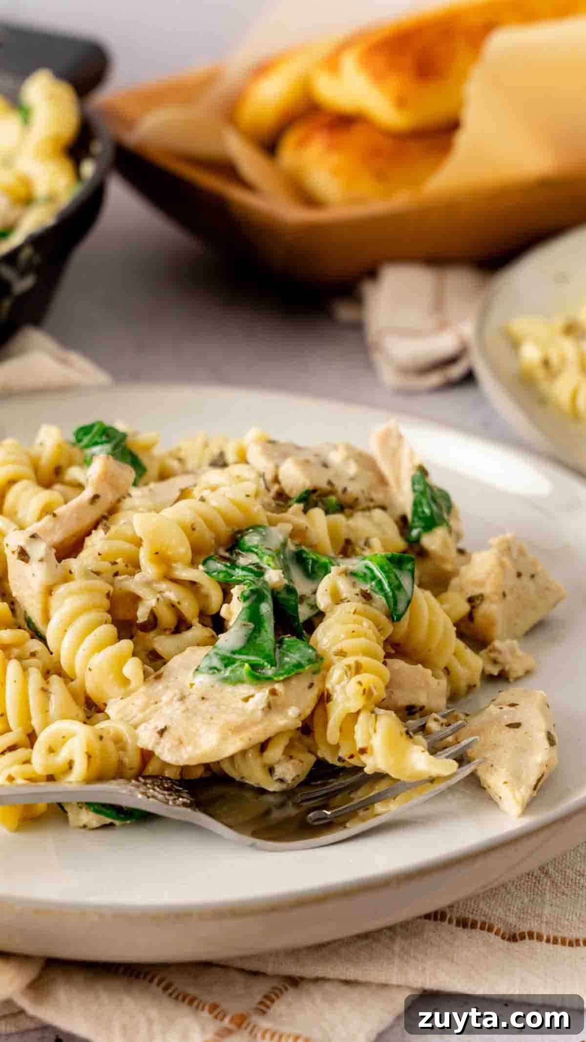 Instant Pot Creamy Pesto Chicken Pasta 6 A plate of chicken pesto pasta tossed with spinach that was made in the Instant Pot with a serving of breadsticks in the background.