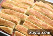 Baked garlic parmesan breadsticks on a large baking sheet with a silicone mat.