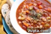 A bowl of pasta fagioli soup on a plate with two slices of Italian French Bread.