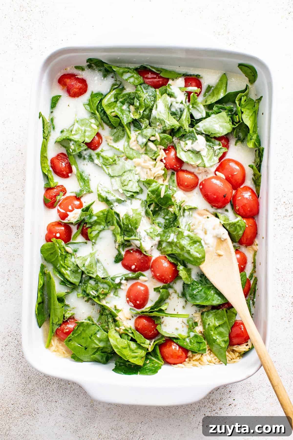 Creamy Boursin Orzo Bake Recipe 6 Baked orzo in a casserole dish with spinach and tomatoes before baking.