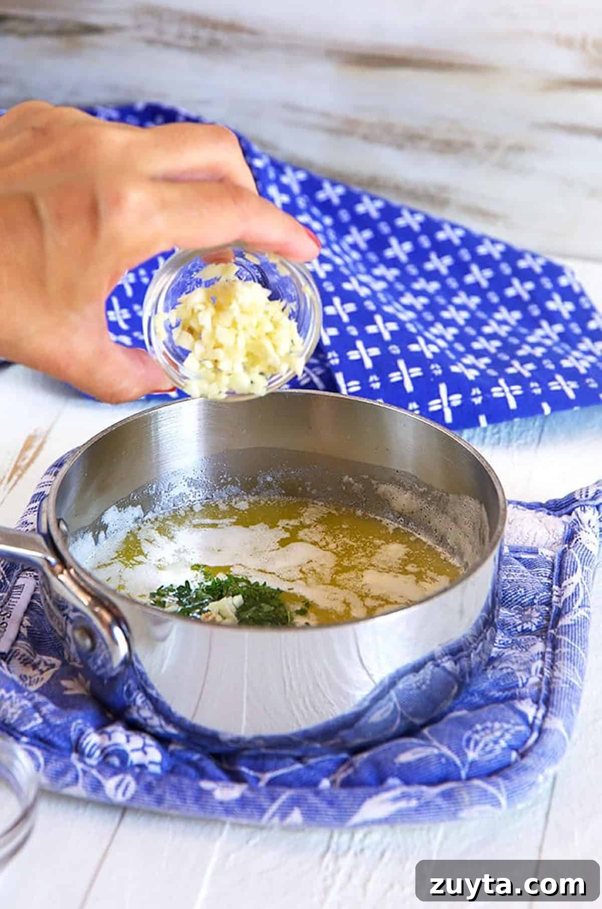 Garlic being poured into a saucepan of melted butter.
