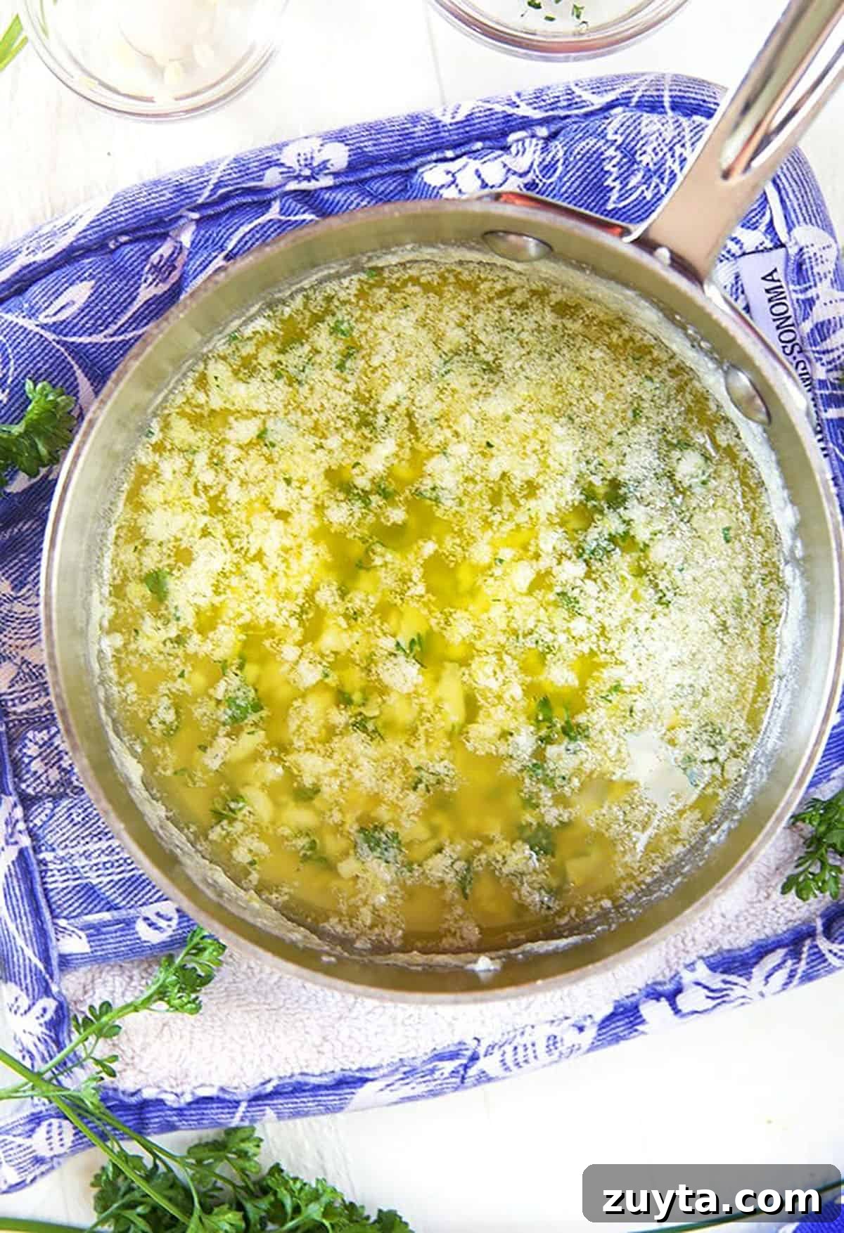 Garlic butter sauce in a saucepan on a blue and white potholder.